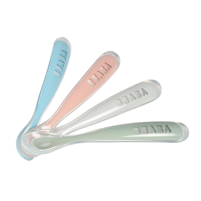 A set of four BEABA First Foods Silicone Spoons is arranged in a fan shape, featuring blue, pink, white, and green handles with the brand name embossed. These spoons are perfect for introducing little ones to their first foods in a fun and simple way.
