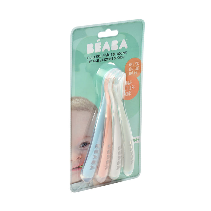 The packaging of BEABAs First Foods Silicone Spoons for infants contains three silicone spoons in pastel blue, white, and pink. The background features a partially visible baby face, with text indicating suitability for first foods at 4 months and up.