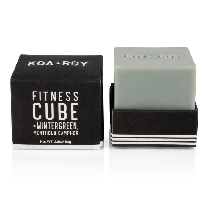 The Fitness Cube bar soap by KOA + ROY features plant-based ingredients like wintergreen, menthol, and camphor for muscle recovery. Its square design is partially visible from its black packaging, with the brand name prominently displayed on both the soap and the box.