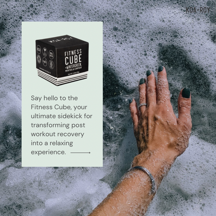 A hand with dark green nail polish rests in foamy water. An inset shows a KOA + ROY Fitness Cube box, highlighting its plant-based ingredients for relaxing, post-workout muscle recovery.
