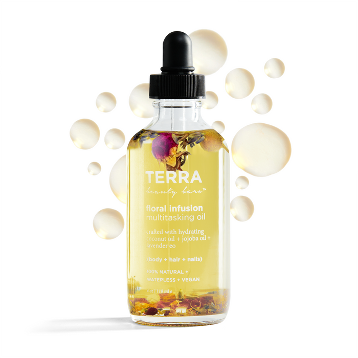 The Terra Beauty Bars Floral Infusion Multitasking Oil for Body + Hair is perfect for self-care, showcased in a clear glass bottle with yellow oil and flower petals inside, and finished with a black dropper cap. Translucent droplets highlight the natural oils.