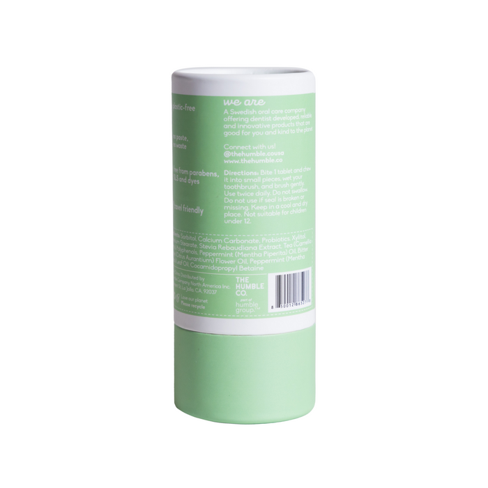 The image shows The Humble Co.s Flouride Free Dental Tabs in a green and white cylinder. This eco-friendly, biodegradable dental care product is convenient for travel and features listed ingredients and benefits on its label.