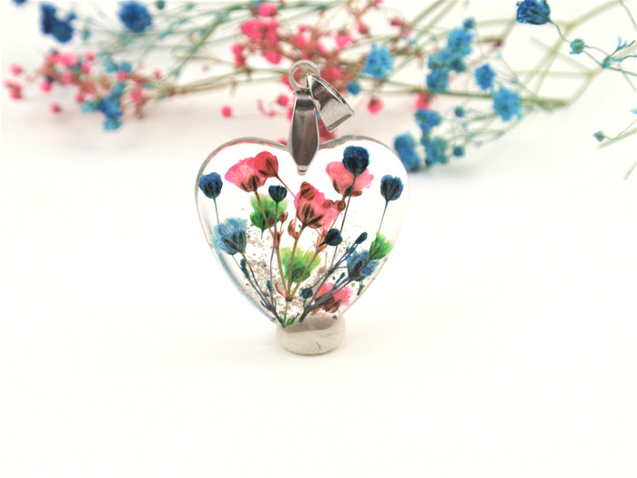 Front view of colorful floral heart pendant with dried flowers and green stems inside clear resin on a silver chain