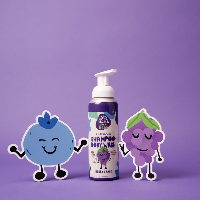 On a purple backdrop, Pacha Soap Co.s Foaming 2-in-1 Shampoo and Body Wash in Beery Grape provides a gentle, non-toxic bath experience. Cartoon blueberry and grape cutouts with smiling faces and limbs add playful charm.