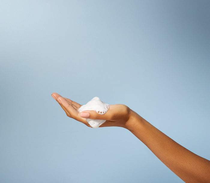 A hand holds a fluffy mound of methods Foaming Body Wash against a light blue backdrop, with the palm up to highlight the texture and volume of this cruelty-free formula.