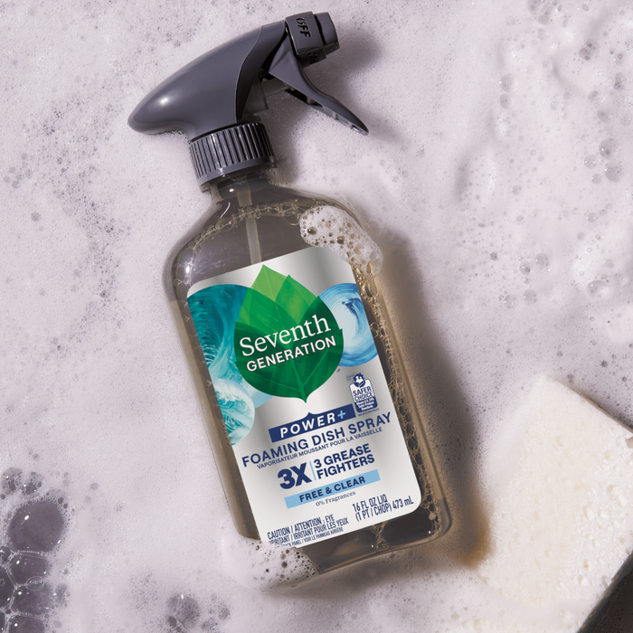 A Foaming Dish Spray from Seventh Generation stands on a bubbly surface with a white sponge. The label emphasizes its 3x Grease Fighter ability, perfect for tough messes with its powerful, clear formula.