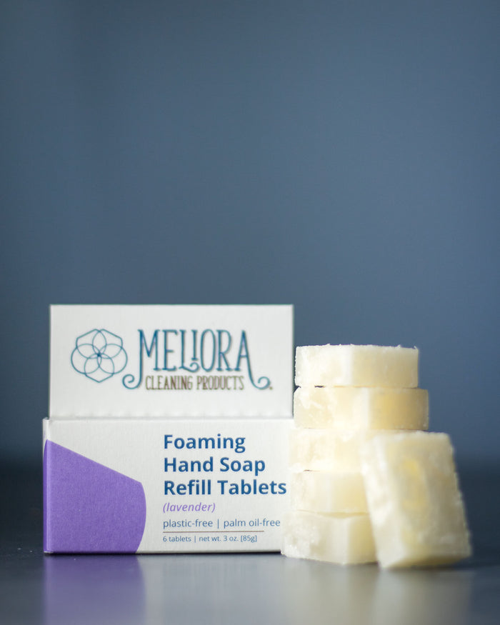 A Meliora box of Foaming Hand Soap Refill Tablets in lavender scent features six white tablets stacked on a gray surface, highlighting its plastic-free and palm oil-free packaging.