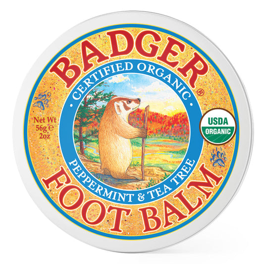 Badger Balms round tin of Foot Balm is perfect for cracked heels, labeled Certified Organic, and offers a refreshing peppermint and tea tree scent. The lid features a badger with a staff against a scenic backdrop, infused with essential oils and proudly displays the USDA Organic logo.