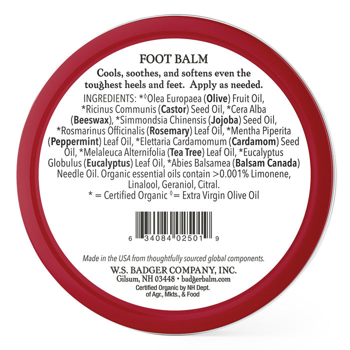 Badger Balms Foot Balm is contained in a red circular tin, ideal for soothing cracked heels. Its label features ingredients like olive oil, castor seed oil, beeswax, and essential oils. Made by W.S. Badger Company in Gilsum, NH, it includes a barcode at the bottom.