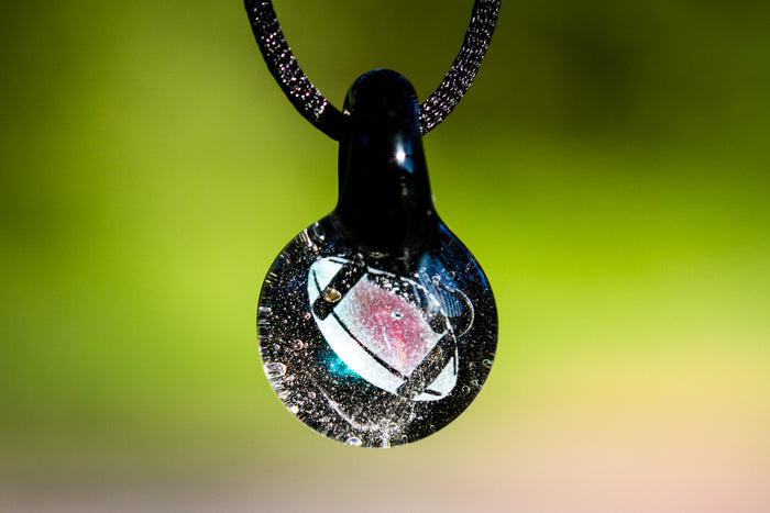 Football hologram pendant infused with cremation ash, a glass charm suspended from a black cord.