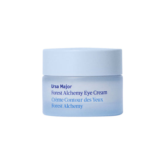 A small, light blue jar of Ursa Major Forest Alchemy Eye Cream—formulated to reduce dark circles and fine lines—rests on a plain white background. The label shows both English and French text.