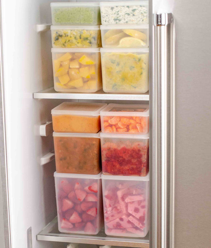 A partially open freezer reveals W&Ps sustainable Freezer Cubes, showcasing an organized storage system with transparent, stackable cubes filled with colorful frozen foods such as vegetable cubes, fruit pieces, and sauces.