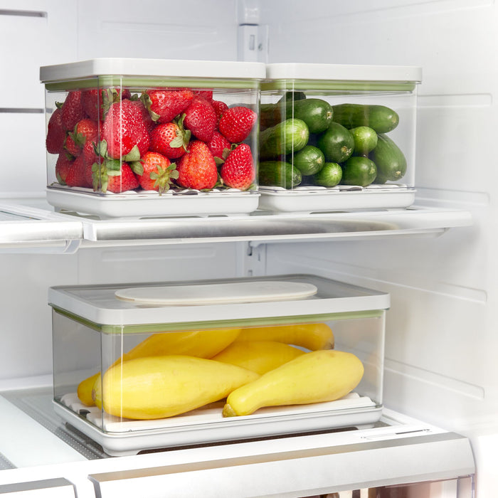 The iDesign Fresh Produce Bin Set, made with recycled plastic, neatly stores strawberries, mini cucumbers, and yellow squash in a refrigerator to extend their shelf life and keep them fresh.