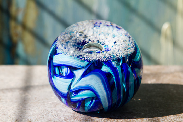 Donut shaped blue glass memorial paperweight infused with cremains featuring white frost on top and bright ribbon swirls