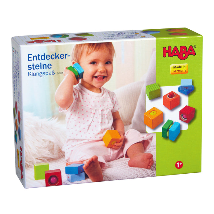 A smiling toddler joyfully explores HABAs eco-friendly Fun with Sounds - Wooden Discovery Blocks, proudly displaying Made in Germany, which encourages sensory development for ages 1 and up.