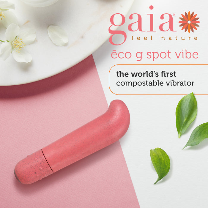 A pink eco-friendly vibrator is displayed on a pink and white surface. Text reads "Gaia Feel Nature, eco g spot vibe, the world's first compostable vibrator." Jasmine flowers and green leaves accentuate the design.