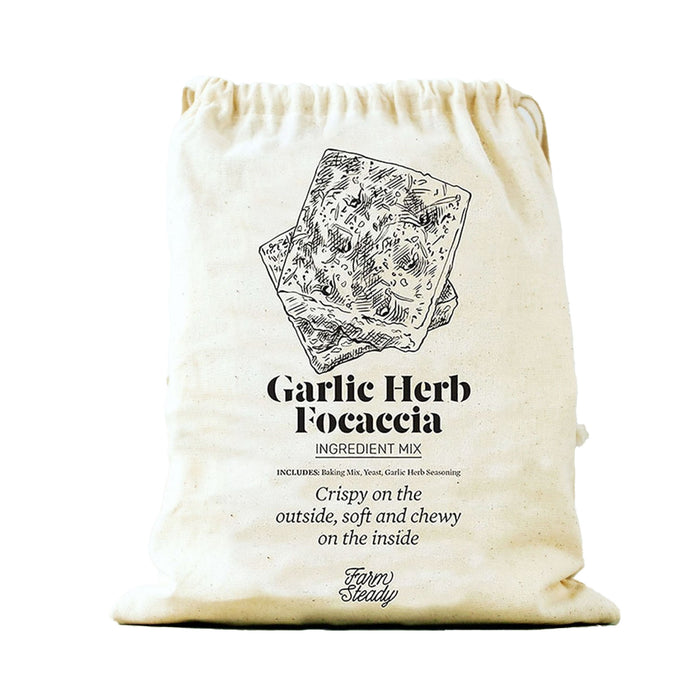 The image shows a beige fabric bag with focaccia bread slices, labeled Garlic Herb Focaccia Baking Mix. It describes the bread as crispy on the outside, soft and chewy on the inside, perfect for garlic and herb lovers by FarmSteady.