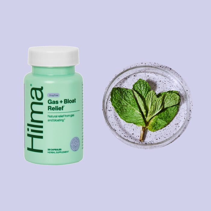 A Hilma Gas + Bloat Relief bottle sits next to a dish of fresh mint leaves. This light green bottle, labeled with natural herbs, provides digestive relief from gas and bloating.