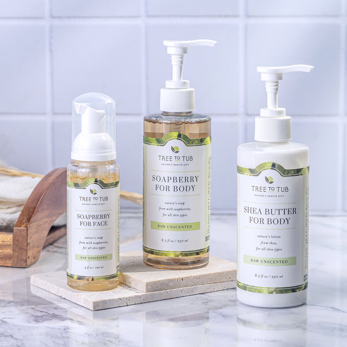 Three Tree To Tub products, including Soapberry for Face (foaming pump), Gentle Body Wash for Sensitive Skin (pump bottle), and Shea Butter for Body, are displayed against a tiled background, elegantly set on a marble-like surface.
