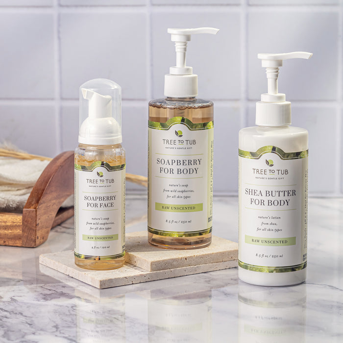 Three Tree To Tub skincare bottles rest elegantly on marble: Gentle Face Wash for Sensitive Skin, Soapberry for Body, and Shea Butter for Body. Perfect for sensitive skin, they feature a minimalist design with labeled text and pump dispensers.