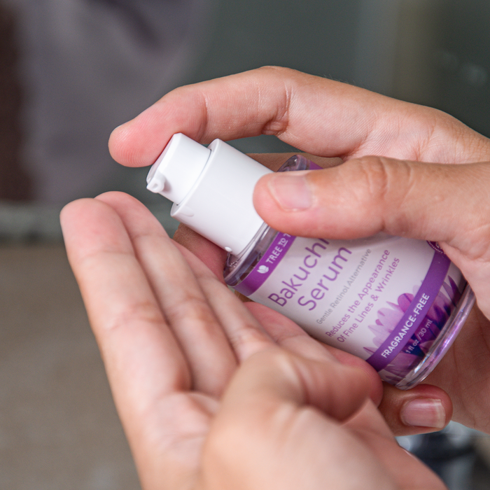 A person dispenses Tree To Tubs Gentle Retinol Alternative Bakuchiol Face Serum from a clear bottle with a white pump and purple-accented label into their hand, highlighting its fragrance-free formula designed to reduce fine lines and wrinkles for smooth, radiant skin.