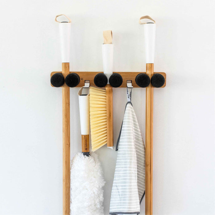 The Full Circle Get A Grip - Mop & Broom Organizer efficiently arranges mops, brooms, and cleaning tools like a white-handled duster, yellow brush, and striped cloth against a white backdrop. This wall-mounted rack keeps your space tidy and organized.