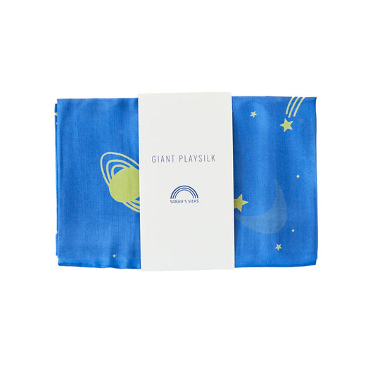 A folded space-themed blue playsilk from Sarahs Silks, adorned with stars, a crescent moon, and planets for open-ended play in Montessori & Waldorf homes. It features a white paper band labeled Giant Playsilk for Open-Ended, Imaginative Play.