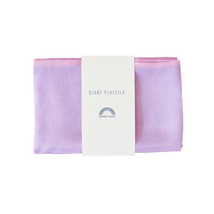 A folded lavender to pink Giant Playsilk from Sarahs Silks, perfect for open-ended play in Montessori & Waldorf homes, features a white label with a rainbow logo reading GIANT PLAY SILK.