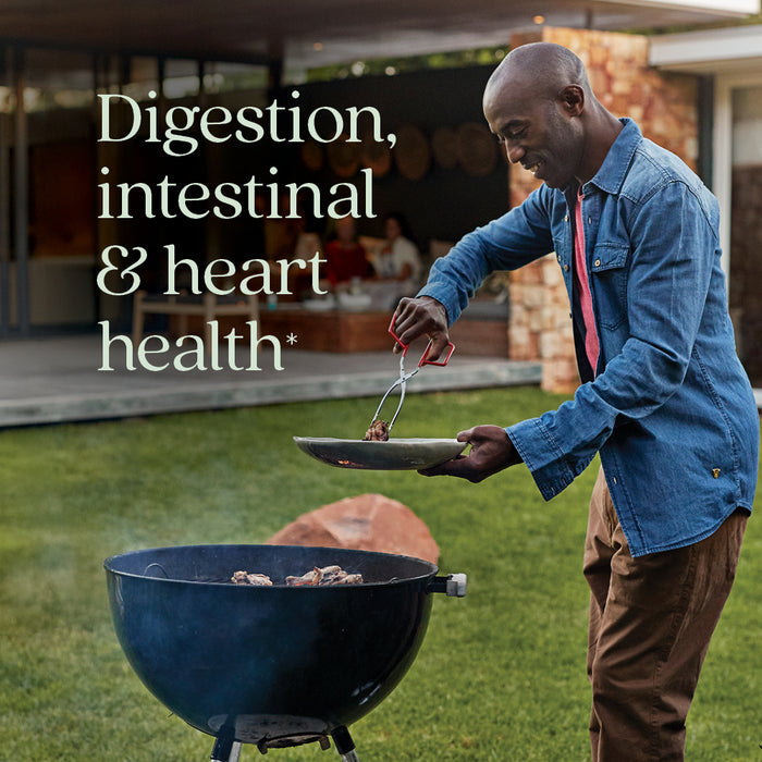 A man grills meat on a barbecue in a backyard while holding a plate. Text reads, Digestion, intestinal & cardiovascular health*. The relaxed outdoor scene showcases New Chapters Ginger Force™ for joint and heart support.