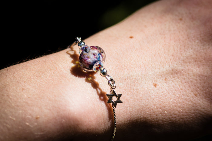 Wrist wearing a glass bead bolo bracelet with cremains and star charm on a silver chain