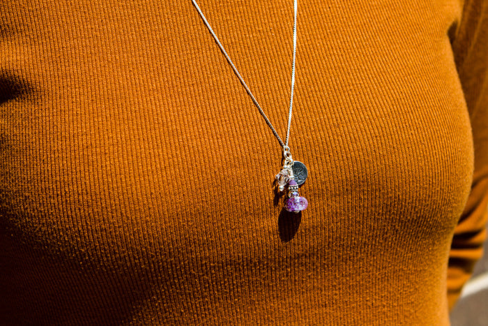Pendant necklace with a purple infused glass bead and charms worn on an orange knit top