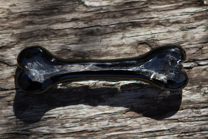 Glossy black glass dog bone with clear interior on weathered wood.