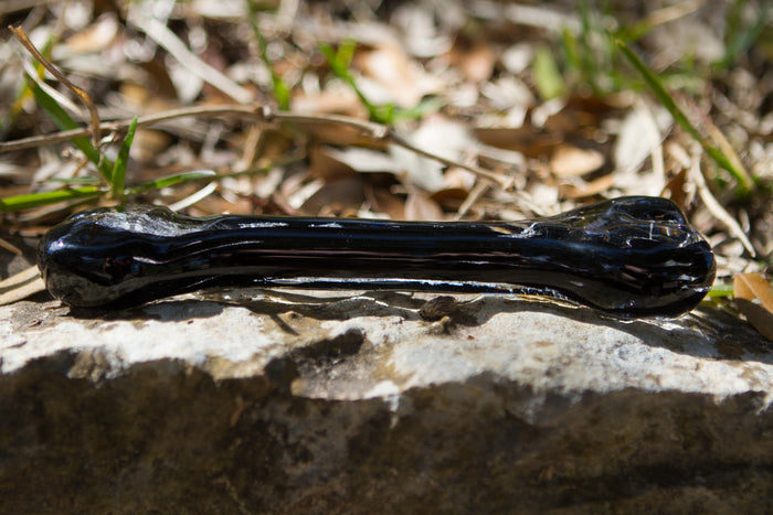 Dark glass dog bone lying on a rough rock surface in sunlight.
