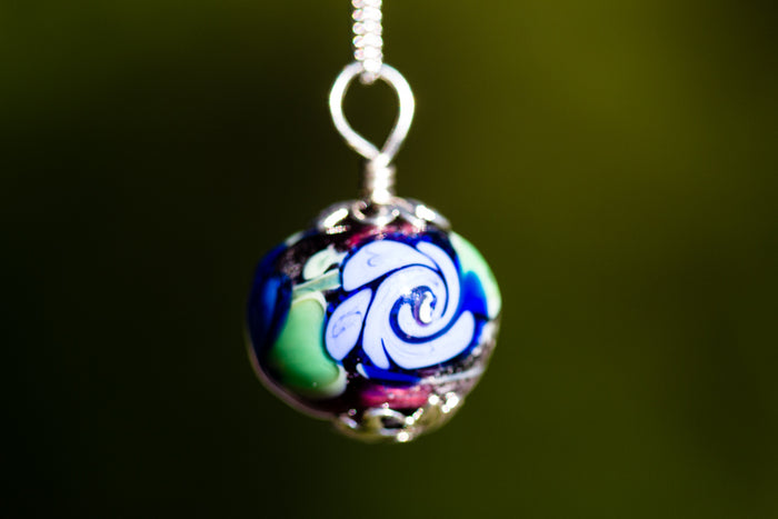 Glass bead pendant with cremains featuring a multicolor swirl in blue green tones on a silver chain