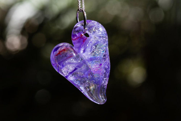 Purple glass heart cremation pendant suspended on a chain with ashes encased inside