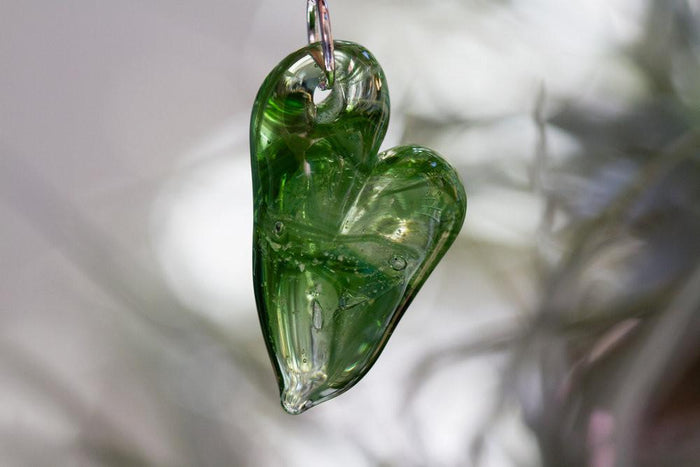 Green glass heart cremation pendant with ash infusion shown in a close up against a soft background