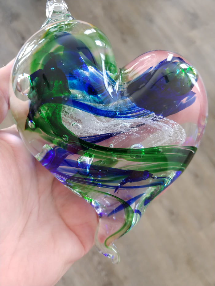 Hanging glass heart infused with cremains in green and blue swirls catching sunlight