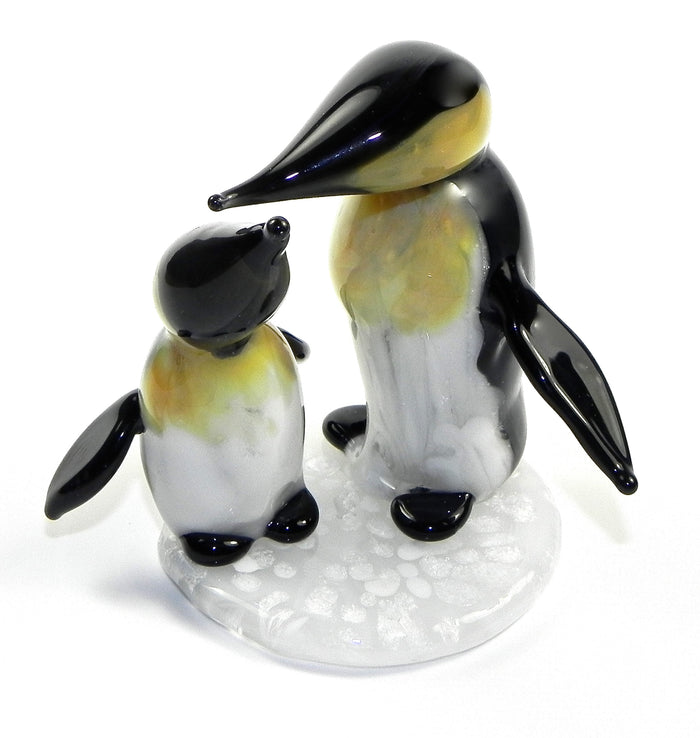 Two glass penguin figurines infused with cremation ashes on a white decorative base.