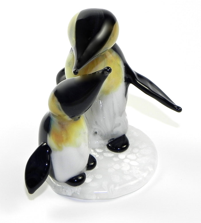 Two glass penguin figurines with cremation ashes featuring yellow and blue marbled detailing on a white base