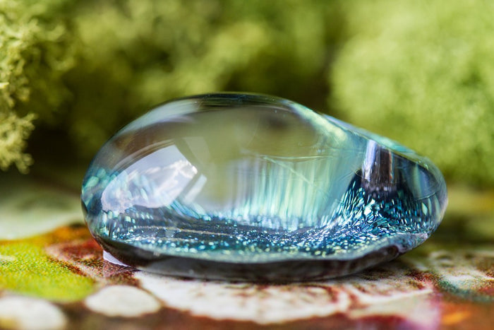 Close-up of a teal blue glass sparkle stone with swirling internal patterns and light reflections
