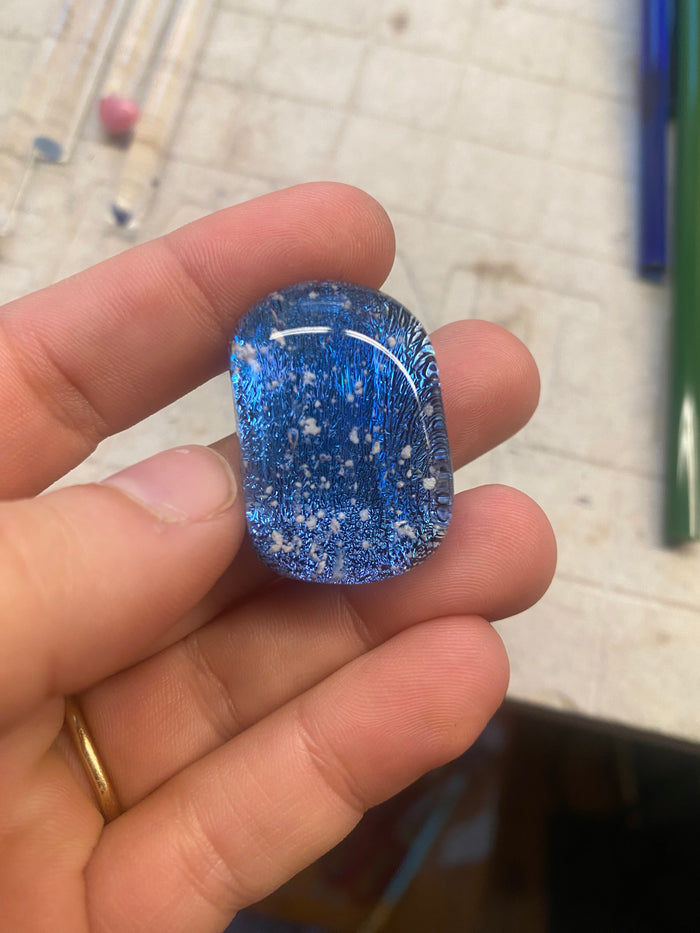 Blue dichroic glass sparkle stone with white specks held between fingers
