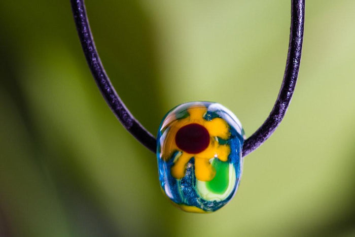 Colorful glass sunflower bead on a dark cord necklace, infused with cremains.
