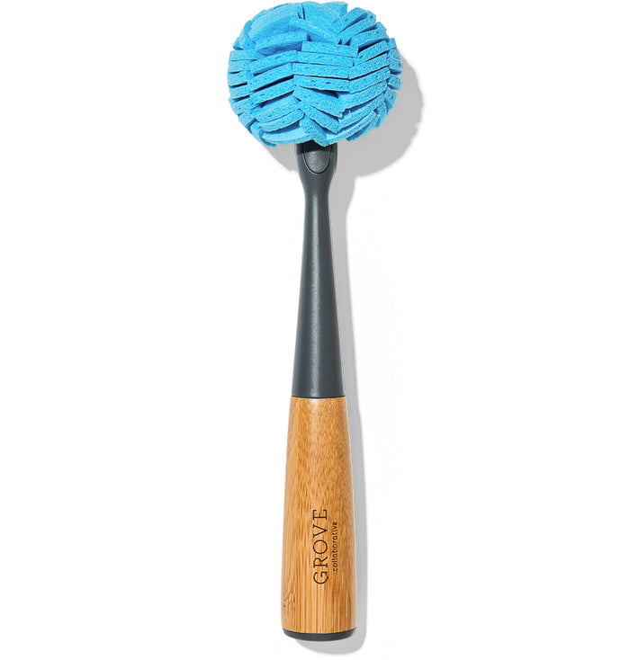 The Grove Co. Glassware Cleaner Replacement Head is a round, blue sponge with a long handle combining wood and gray plastic, branded GROVE.” It effortlessly wipes away lipstick stains, and its sleek design stands out against the white background.