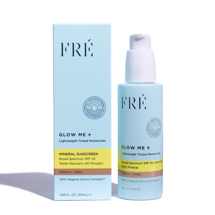 A bottle of GLOW ME + Tinted Mineral SPF 30 Moisturizer by FRÉ Skincare elegantly stands in front of its box, highlighting its medium-deep tint and 40-minute water resistance, enriched with Argania Active Complex™. Volume: 1.69 fl oz (50 ml).
