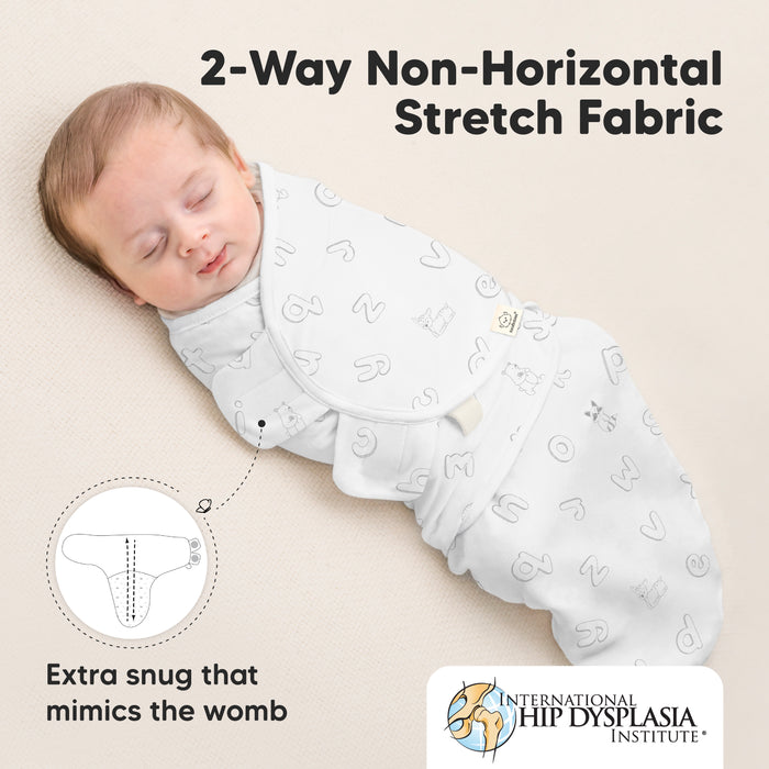 A baby is sleeping peacefully wrapped in a swaddle with alphabet designs. The text highlights "2-Way Non-Horizontal Stretch Fabric" and mentions that it's "Extra snug that mimics the womb." The International Hip Dysplasia Institute logo is visible.