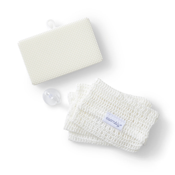 The GoTwo™ Kitchen Sponge Set by Esembly Baby features a textured white mat, folded mesh cloth with a label, and a looped transparent button, all elegantly minimalist on a white background. This sustainable sponge set combines style and functionality.