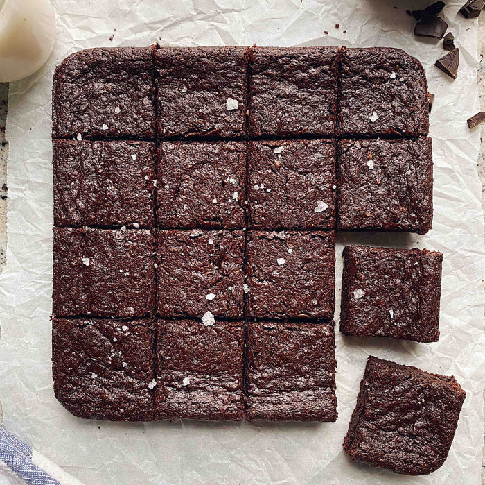 Sixteen mouthwatering brownies crafted from Stellar Eats’ Grain-Free Fudge Brownie Mix, made with almond flour, lie on crumpled parchment. Each gluten-free brownie is sprinkled with sea salt, with two pieces slightly apart, tempting a taste test.