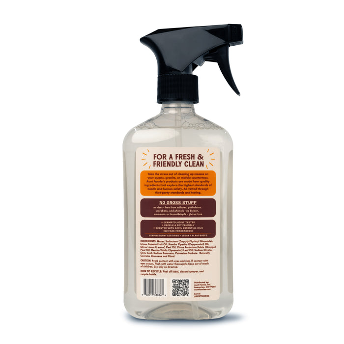 The back of the transparent spray bottle from Aunt Fannies features a black nozzle and a label highlighting cleaning benefits with essential oils and natural surfactants. It promises a fresh & friendly clean as the perfect Granite + Stone Cleaner, with a QR code visible at the bottom.