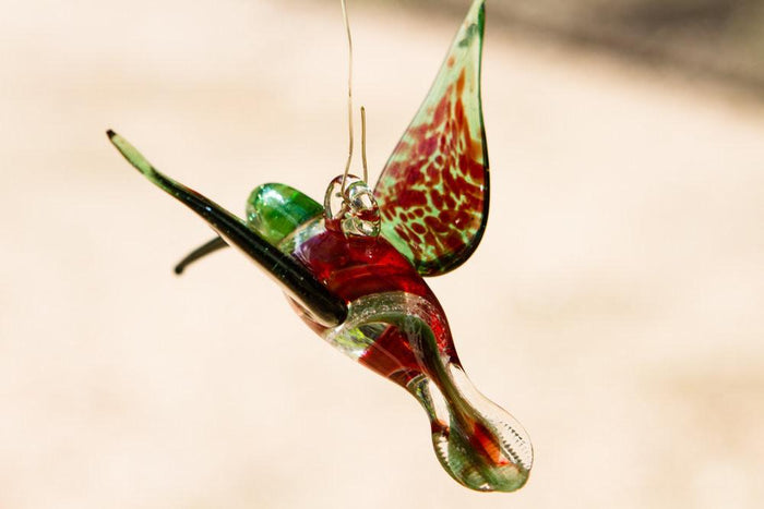 Hummingbird ornament in green and red glass with ashes swirled through the body and a hanging hook.