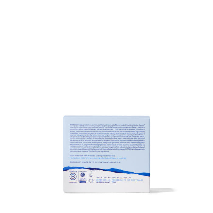 A blue and white rectangular box of Ursa Major Green Slate Mineral Polish is shown from the back, with text and logos highlighting natural exfoliants, certifications, and recycling info. The plain white background complements the clean design.